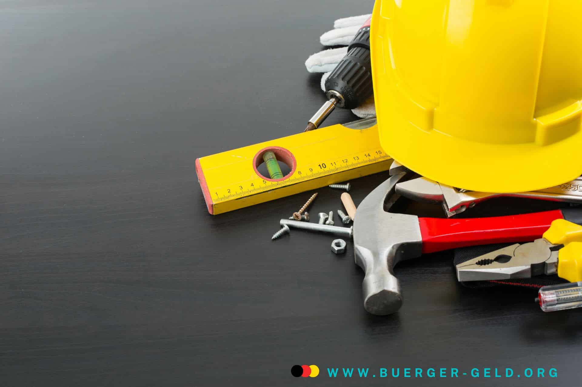 Was das Bürgergeld nicht ist! 2 Werkzeuge und Bauarbeiterhelm liegen auf einer Tischplatte