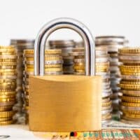 Gibt es zu wenig Sanktionen beim Bürgergeld? 4 Stapel Euro Münzen auf 50 Euro Schein mit Vorhängeschloss davor