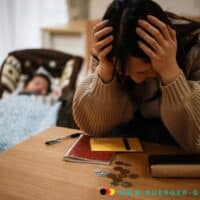 Unterhaltsvorschuss Auszahlung Oktober - wann kommt der Zuschuss? 4 Mutter sitzt traurig über Kleingeld gebeugt am Tisch, Kind schläft im Hintergrund