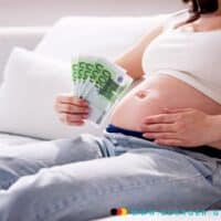 Schwanger – welche Familienleistungen kann ich beantragen? 5 Schwangere Frau hält ihren Bauch und hundert Euro Scheine