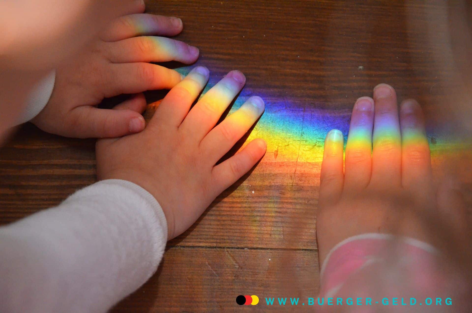 Kindergrundsicherung gescheitert – oder kommt sie 2025 doch noch? 2 Kinderhände versuchen einen leuchten Regenbogen auf einem Holzuntergrund zu fassen