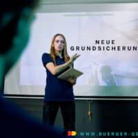 Neue Grundsicherung statt Bürgergeld – das will die CDU 4 Frau zeigt auf Plakat hinter sich mit Aufschrift: Neue Grundsicherung