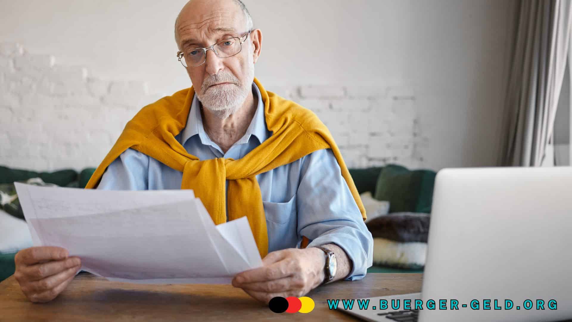 Älterer Mann sitzt am Tisch in einem Wohnzimmer, trägt ein hellblaues Hemd und einen gelben Pullover über den Schultern. Er hält mehrere Dokumente in der Hand und schaut auf Papiere, vor ihm steht ein Laptop. Im Hintergrund ist ein Sofa und eine helle Wand zu sehen. Unten rechts befindet sich das Logo von buerger-geld.org.