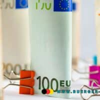 Flexirente – So gelingt der flexible Übergang in den Ruhestand 5 Mehrere aufgerollte Euro-Geldscheine in verschiedenen Stückelungen, die mit farbigen Büroklammern fixiert sind; im Vordergrund ein 100-Euro-Schein, im Hintergrund weitere 50- und 200-Euro-Scheine; unten rechts das Logo und die Internetadresse www.buerger-geld.org.