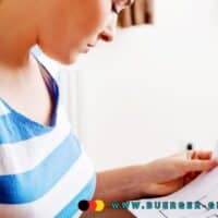 Angemessenheit der Wohnkosten nach der Karenzzeit: Was Bürgergeld-Empfänger jetzt wissen müssen 4 Junge Frau im blau-weiß gestreiften T-Shirt betrachtet einen Wohnungsgrundriss auf Papier in heller Wohnung.