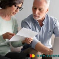 Rentenantrag: Diese Fehler bei der Krankenversicherung können teuer werden 4 Älteres Paar sitzt gemeinsam auf dem Sofa, betrachtet Unterlagen und arbeitet am Laptop. Im Vordergrund sind Papiere und eine Kreditkarte zu sehen, unten rechts ist die Webadresse www.buerger-geld.org eingeblendet.