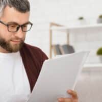 Mann liest aufmerksam offizielle Rentenunterlagen im Wohnzimmer, daneben Logo von Bürger & Geld.