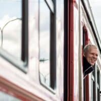 Deutschlandticket 2025: Rentner fahren jetzt deutlich günstiger – Jetzt noch den Rabatt sichern 4 Person blickt aus dem Fenster eines fahrenden Zuges; Ansicht von außen mit sichtbaren Stromleitungen und Logo von Bürger & Geld unten rechts.