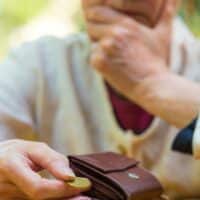 Rentenverlierer: Diese Jahrgänge bekommen am wenigsten Geld! 4 Ältere Frau hält eine einzelne Münze über ihrem fast leeren Portemonnaie und blickt besorgt – Symbolbild für geringe Rente und drohende Altersarmut, illustriert für Bürger & Geld.