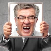 Pflichtjahr für Rentner: Zwangsdienst im Ruhestand - ein Angriff auf die Freiheit? 5 Älterer Mann im Anzug hält einen leeren Bilderrahmen vor seinem Gesicht, Symbol für Identität und kontroverse Debatte um das Pflichtjahr für Rentner, vor grauer Wand mit Bürger & Geld Logo.