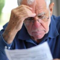 Warum wird die Rente besteuert? Alles, was Sie jetzt wissen müssen 5 Senior betrachtet nachdenklich seinen Rentenbescheid und prüft Abzüge, daneben das Logo von Bürger & Geld.