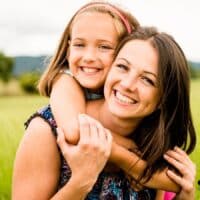 So reich belohnt der Staat Eltern für ihre Kindererziehung in der Rente 4 Mutter mit Kind auf dem Arm in einer grünen Wiese – Symbolbild für Eltern, die ihre Kinder selbst erziehen und auf eine Berufstätigkeit verzichten, Fokus auf Rente für Eltern ohne Erwerbstätigkeit.