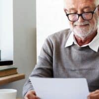 Neue Rentenregeln 2026: Vorteile für Schwerbehinderte im Überblick 4 Älterer Mann liest konzentriert einen Brief am Schreibtisch, im Vordergrund Pflanzen und Bücher; Bildsymbol für vorzeitige Rente für schwerbehinderte Menschen ab 2026.