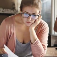 3.000 € brutto, und dann? So wenig Rente bleibt tatsächlich übrig 4 Eine Frau sitzt nachdenklich am Schreibtisch und betrachtet Unterlagen zur Rentenberechnung. Im Vordergrund liegt ein Taschenrechner, im Hintergrund erkennt man einen Mann und eine Küche. Das Logo von Bürger & Geld ist unten rechts eingeblendet.