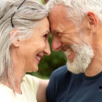 Deutschlands Rente ist stabiler, als viele glauben – warum die Panik unbegründet ist 4 Älteres glückliches Paar lächelt sich an, steht Stirn an Stirn im Grünen – Symbol für sichere und stabile gesetzliche Rente in Deutschland 2025