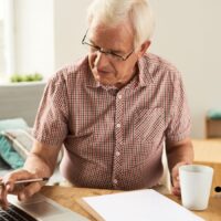 Doppelte Rentenbesteuerung: Wann Rentner 2026 Geld zurückbekommen könnten 4 Älterer Mann überprüft Rentenunterlagen am Laptop zu Hause – Thema doppelte Rentenbesteuerung und mögliche Rückzahlungen ab 2026, Symbolbild für Bürger & Geld.