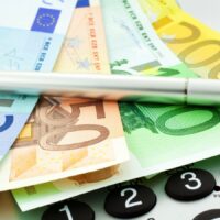 Ab 2026 steigen die Sozialabgaben spürbar – wer jetzt betroffen ist und mehr zahlen muss 5 Euro-Banknoten, Stift und Taschenrechner – höhere Sozialabgaben und sinkendes Nettoeinkommen ab 2026