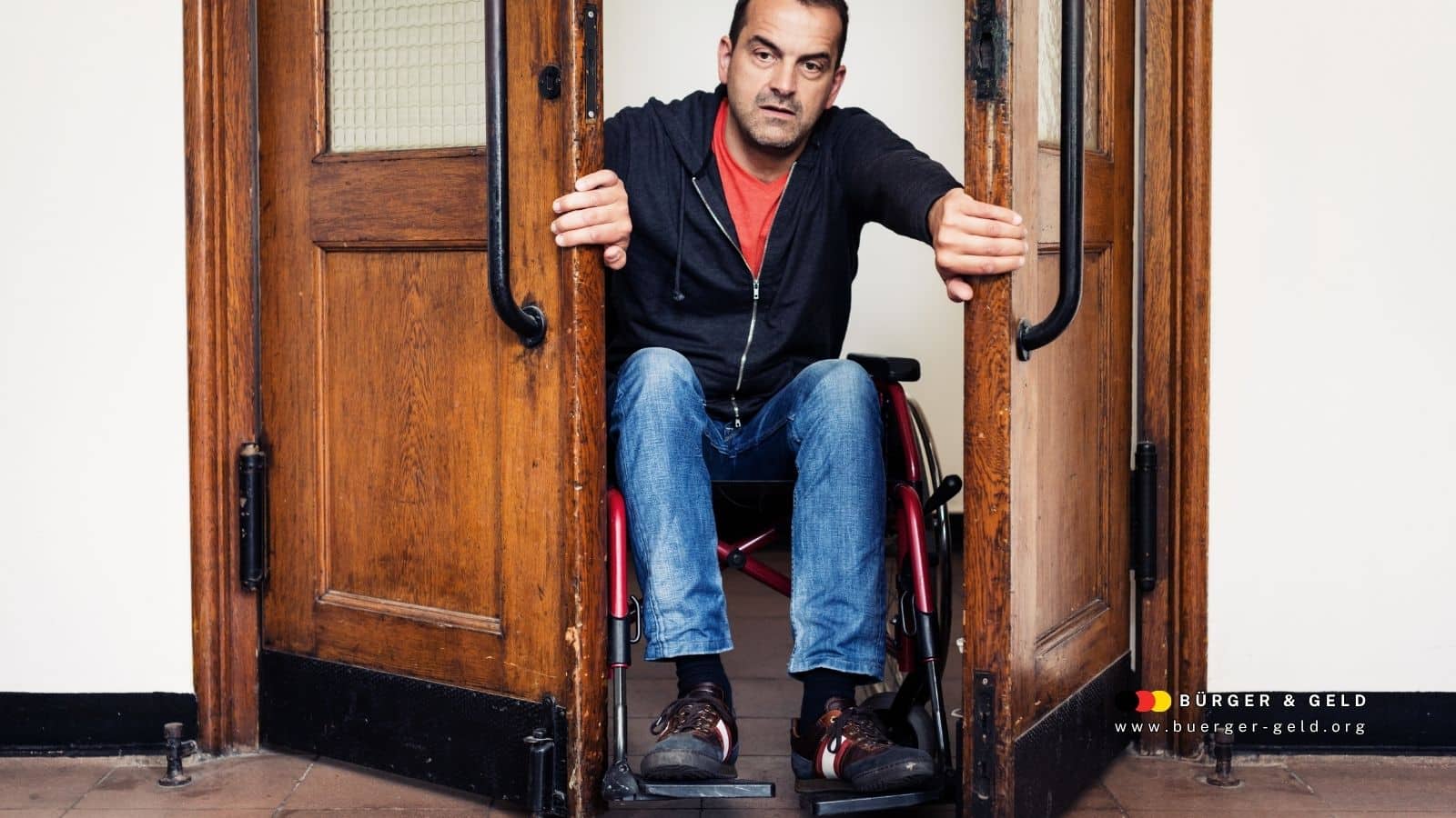 Mann im Rollstuhl öffnet schwere Holztüren in einem öffentlichen Gebäude – Symbolbild für Barrierefreiheit und den Anspruch auf Merkzeichen G bei untypischen Erkrankungen