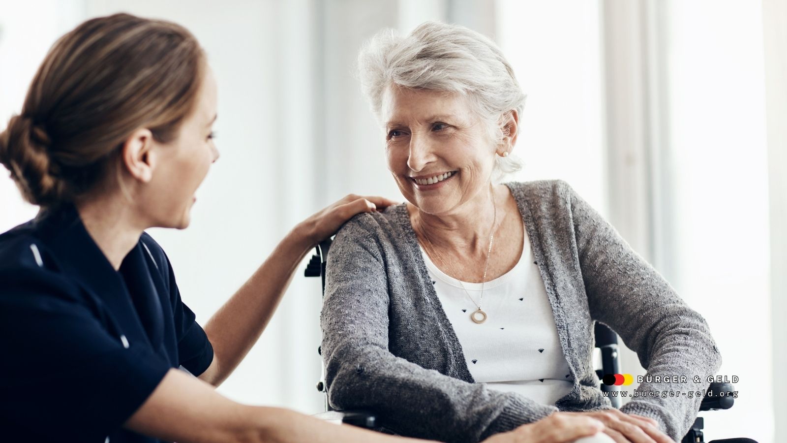 Ältere Frau im Rollstuhl lächelt eine Pflegekraft an – Symbolbild für Pflegegrad 2 und familiäre Unterstützung bei der häuslichen Pflege in Deutschland.