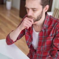 Bis zu 300 Euro mehr Rente durch das Formular V0100 4 Ein Mann in kariertem Hemd sitzt nachdenklich vor einem Laptop am Schreibtisch im Wohnzimmer.