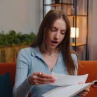 Bürgergeld nicht verschenken: Wie ein fristwahrender Antrag bares Geld schützt! 5 Junge Frau sitzt überrascht auf dem Sofa und hält einen Bürgergeld-Bescheid in der Hand – Symbolbild für fristwahrende Antragstellung und gesicherte Sozialleistungen.