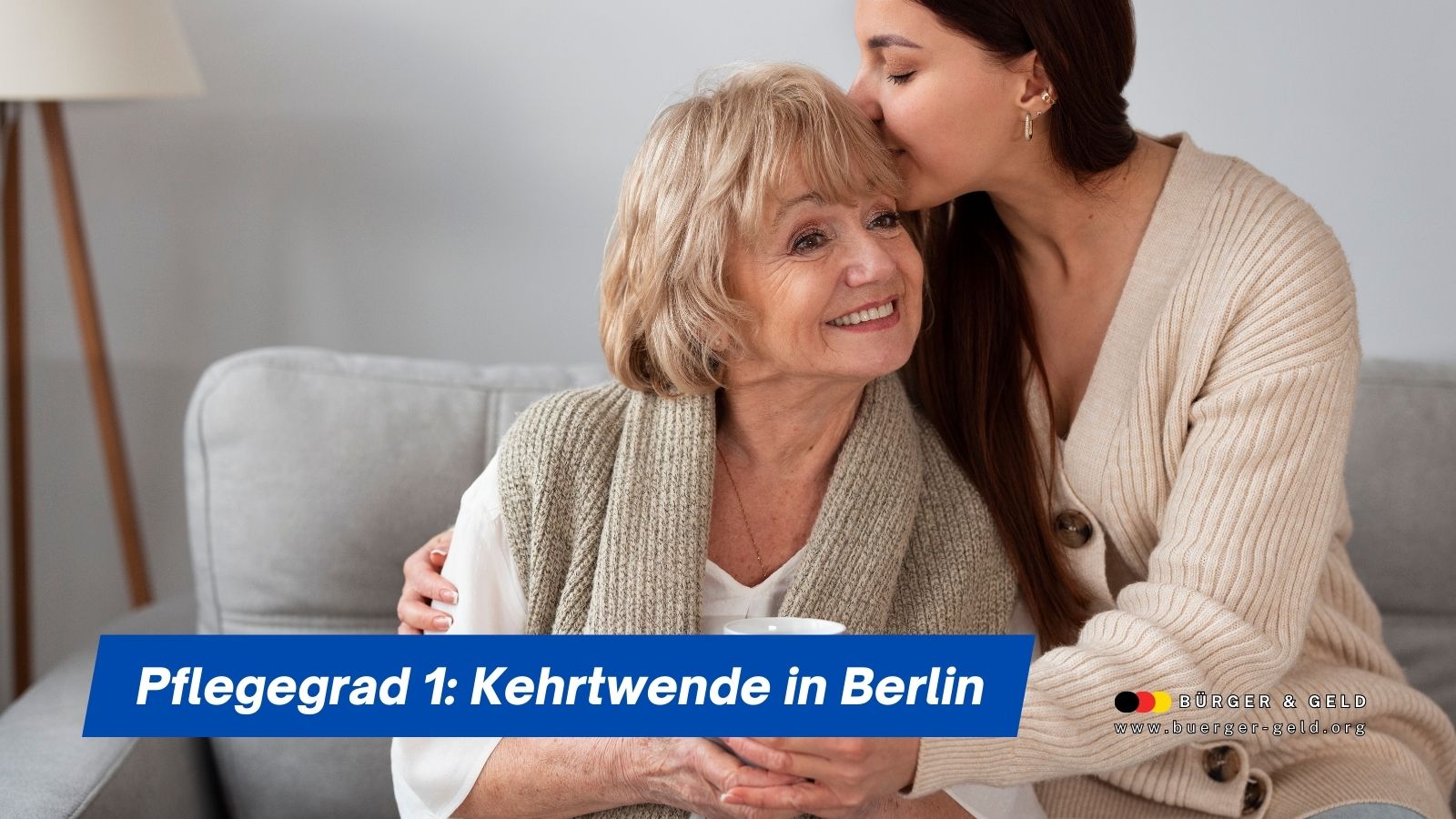 Ältere Frau sitzt lächelnd auf dem Sofa, ihre erwachsene Tochter umarmt sie liebevoll – Symbolbild für Angehörige, die von der Kehrtwende beim Pflegegrad 1 in Berlin profitieren.