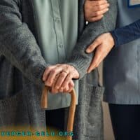 ältere Person wird von jüngerer Person am Arm gehalten