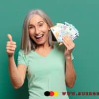 Seniorin mit grauen Haaren hält mehrere Euro-Geldscheine in der Hand und zeigt Daumen hoch vor grünem Hintergrund. Unten rechts ist das Logo und die Webadresse von buerger-geld.org zu sehen.