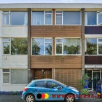 Dreistöckiges Mehrfamilienhaus mit mehreren Wohnungen, davor zwei geparkte Autos und ein Baum, auf dem vorderen Auto sowie im Bild unten das Logo und die Webadresse von buerger-geld.org.