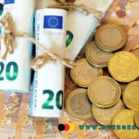 Mehrere gefächerte 50-Euro-Geldscheine, auf denen zusammengerollte 20-Euro-Scheine mit Kordel liegen, daneben Stapel von Euro-Münzen; im Vordergrund die Adresse www.buerger-geld.org in blauer Schrift