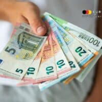 Eine Hand hält mehrere Euro-Geldscheine (5, 10, 20, 50, 100 Euro) fächerförmig, Symbolbild für Rentenlücken durch lange Schul- und Studienzeiten sowie freiwillige Beitragsnachzahlung zur gesetzlichen Rentenversicherung bis zum 45. Lebensjahr, mit Logo von Bürger & Geld – Nachrichtenmagazin des Vereins Für soziales Leben e. V.