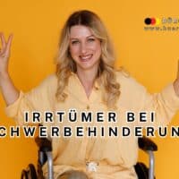 Frau im gelben Hemd sitzt im Rollstuhl vor gelbem Hintergrund und zeigt mit beiden Händen das Victory-Zeichen; Text „Irrtümer bei Schwerbehinderung“ weist auf häufige Missverständnisse zum Thema Schwerbehinderung im Arbeitsleben hin; Bildmotiv für Aufklärung und Inklusion.