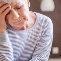 Ältere Frau in gestreiftem Pullover sitzt nachdenklich im Zimmer – Thema Rente und mögliche Hürden beim Ruhestand