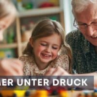 Ältere Person spielt gemeinsam mit zwei Kindern an einem Tisch voller bunter Bausteine in einem hellen Raum; Symbolbild für den Generationendialog und gesellschaftlichen Zusammenhalt.
