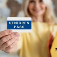 Eine Seniorin hält einen blauen Seniorenpass in die Kamera. Der Fokus liegt auf dem Seniorenpass, im Hintergrund ist die Person unscharf zu sehen. Unten rechts ist das Logo von BÜRGER & GELD sowie die Website-Adresse eingeblendet