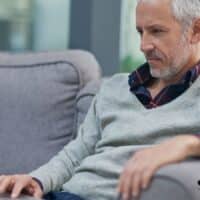 Älterer Mann sitzt entspannt auf dem Sofa und informiert sich mit dem Laptop über Rentenplanung und Sozialversicherung auf Bürger & Geld.