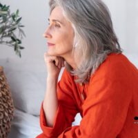 Ältere Frau mit grauen Haaren sitzt nachdenklich auf dem Sofa, symbolisiert Sorge um Witwenrente ab Dezember 2025 – Bürger & Geld