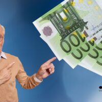 Älterer Mann mit Brille zeigt auf mehrere 100-Euro-Scheine, Symbolbild für steuerfreie Rente ab 2026 bis zu 49.000 Euro, Bürger & Geld Magazin