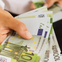 Hand hält mehrere 100-Euro-Geldscheine – symbolisiert zusätzliche Leistungen und finanzielle Unterstützung zum Bürgergeld 2026 in Deutschland.