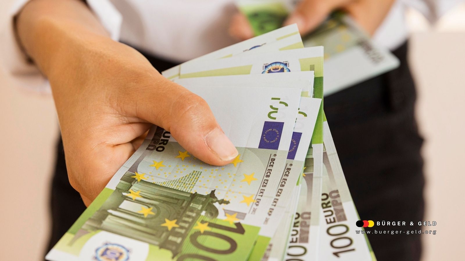 Hand hält mehrere 100-Euro-Geldscheine – symbolisiert zusätzliche Leistungen und finanzielle Unterstützung zum Bürgergeld 2026 in Deutschland.
