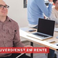 Ein Mann im Rollstuhl sitzt an einem Schreibtisch in einem modernen Büro. Im Hintergrund arbeiten zwei Kollegen an Laptops. Auf dem Bild steht der Text „Hinzuverdienst EM Rente“. Rechts unten ist das Logo von Bürger & Geld und die Internetadresse zu sehen.