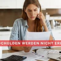 unge Frau sitzt besorgt am Küchentisch, hält einen Brief mit Rechnungen in der Hand, spricht am Telefon und um sie herum liegen Unterlagen, Taschenrechner und Laptop. Im Bild ist eine rote Infobox mit der Aufschrift „Diese Schulden werden nicht erlassen“ sowie das Logo von Bürger & Geld.