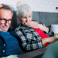 Älteres Ehepaar sitzt nachdenklich im Bett, betrachtet besorgt den Laptop – sie erkennen typische Versicherungsfehler für Rentner, die viel Geld kosten.
