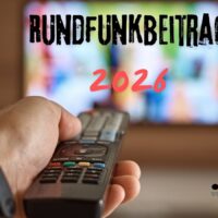 Hand hält Fernbedienung vor einem TV-Bildschirm mit der Aufschrift „Rundfunkbeitrag 2026“ – Bürger & Geld informiert über die Zukunft des Rundfunkbeitrags.