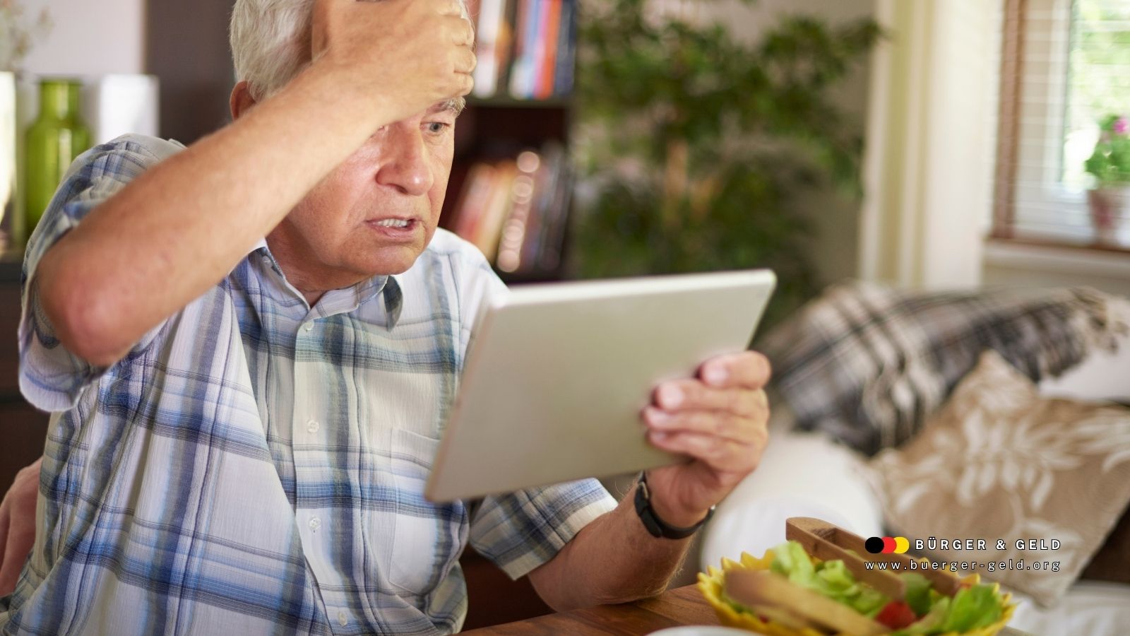Älterer Mann sitzt nachdenklich am Tisch, hält ein Tablet in der Hand und blickt sorgenvoll darauf; im Vordergrund eine Schale mit Salat, im Hintergrund ein gemütlich eingerichtetes Wohnzimmer mit Licht und Pflanzen. Zu sehen ist das Logo des Nachrichtenmagazins „Bürger & Geld“.