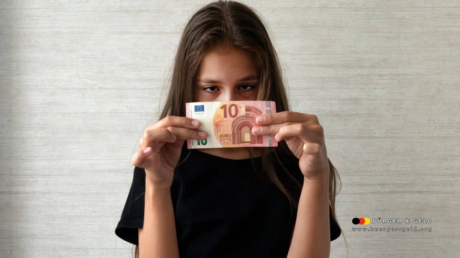 Junge Frau mit langen braunen Haaren hält einen Geldschein in beiden Händen; ihr Gesicht ist unkenntlich gemacht. Im Vordergrund steht das Thema Kindergeld; unten rechts ist das Logo des Nachrichtenportals BÜRGER & GELD zu sehen.