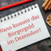 Notizbuch mit der Aufschrift „Wann kommt das Bürgergeld im Dezember?“; winterliche Deko mit Zimt, Trockenfrucht und Tannenzweigen; Logo „Bürger & Geld“ links unten.