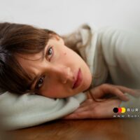 Frau liegt erschöpft und nachdenklich auf dem Tisch – Symbolbild für die Belastung durch psychische Erkrankungen bei körperlichen Behinderungen, Bürger & Geld Nachrichtenmagazin