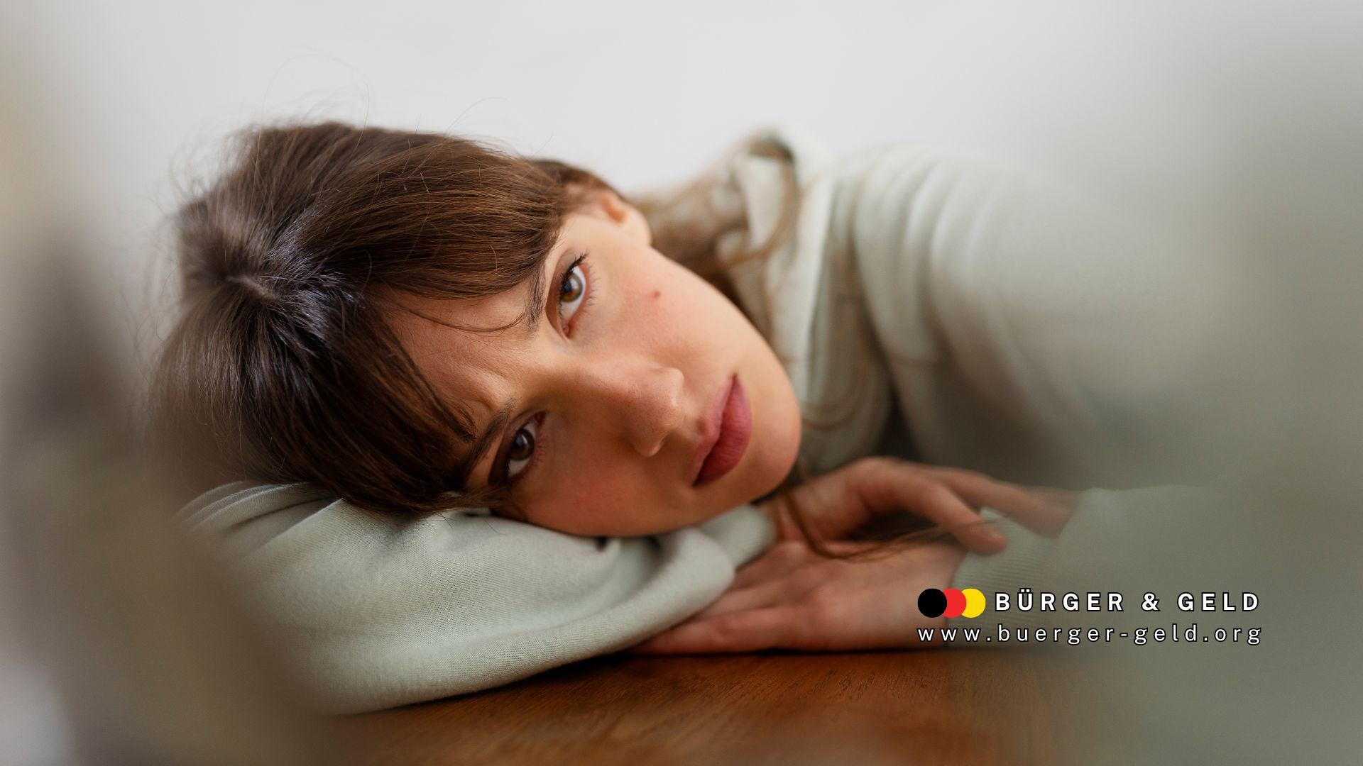 Frau liegt erschöpft und nachdenklich auf dem Tisch – Symbolbild für die Belastung durch psychische Erkrankungen bei körperlichen Behinderungen, Bürger & Geld Nachrichtenmagazin