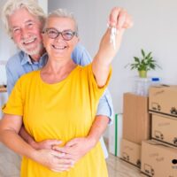 Rente und Wohngeld: Warum Rentner ihr Wohngeld nicht beantragen 5 Älteres Paar umarmt sich im neuen Zuhause mit Umzugskartons und hält symbolisch einen Wohnungsschlüssel – Rentner mit Wohnproblemen und Wohngeld-Anspruch.